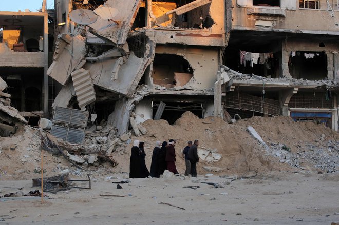 Palestinci pred uničenimi stavbami v Gazi FOTO: AFP