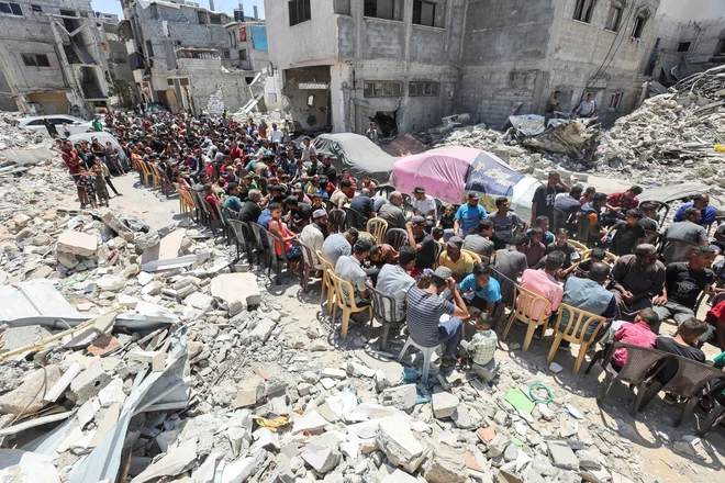 Palestinci jedo hrano, ki jo je pripravila dobrodelna kuhinja v bližini hiš, uničenih v izraelski vojaški ofenzivi, v mestu Khan Younis na jugu Gaze. Predsednik ZDA Joe Biden je povedal, da je Izrael predlagal nov celovit sporazum o prekinitvi ognja v Gazi za šest tednov, če Hamas izpusti vse talce, ki jih je zajel med napadom na Izrael 7. oktobra lani. Pozval je h koncu vojne. Foto: Ramadan Abed/Reuters