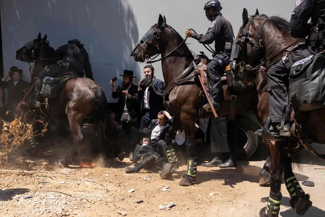 Pred vojaško bazo Tel HaShomer blizu Tel Aviva izraelska policija obkroža protestnike med demonstracijami ultraortodoksnih Judov na prvi dan, ko so morali verni judovski moški po sodni odločbi na obvezno služenje vojaškega roka. Ultraortodoksni semeniščniki, ki so bili v preteklosti izvzeti iz obveznega služenja vojaškega roka, so vpoklicani, ker izraelska vojna v Gazi in morebitni spopad s Hezbolahom na severni meji zmanjšujeta sredstva in spodbujata odpor do tistih, ki jim ni treba služiti. Foto: Oren Ziv/Afp