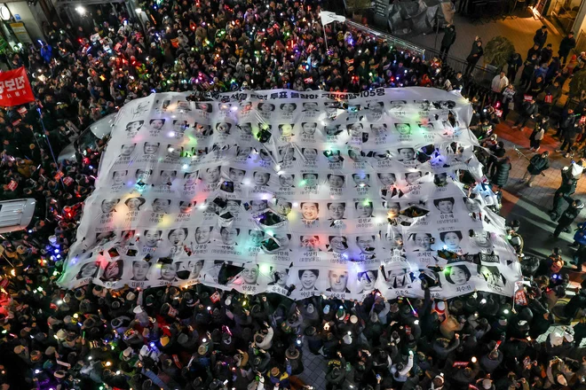 Protestniki so se pred sedežem stranke v Seulu udeležili svečane vigilije z zahtevo po odstavitvi južnokorejskega predsednika Yoona Suk Yeola. V zrak držijo transparent, ki obsoja poslance Stranke ljudske moči, ki niso sodelovali pri glasovanju za Yoonovo odstavitev. Vodja južnokorejske opozicije je danes opozoril kolege iz vladajoče stranke, da se bo zgodovina spominjala, če ne bodo podprli obtožbe Yoona. Do glasovanja o njegovi odstavitvi s položaja je le še 24 ur. Yoonov neuspešen poskus uvedbe prvega vojnega stanja v Južni Koreji po več kot štirih desetletjih, je živahno in bojevito demokracijo v državi pahnil v najhujši politični pretres v zadnjih letih. Foto - Afp