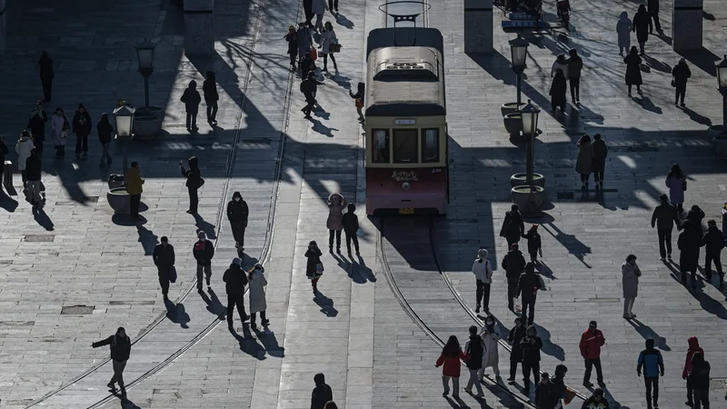 Ljudje se sprehajajo po ulici Qianmen v Pekingu. Kljub zniževanju plač in zamudam z izplačili v zadnjem času ostaja služba v javni upravi zaradi varnosti in ugodnosti privlačna za mlade Kitajce, saj se jih je za nacionalni izpit, ki odpira vrata do 40.000 delovnih mest, prijavilo rekordnih 3,4 milijona. Foto: Jade Gao/Afp
