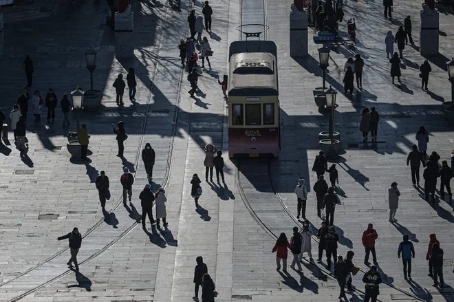Ljudje se sprehajajo po ulici Qianmen v Pekingu. Kljub zniževanju plač in zamudam z izplačili v zadnjem času ostaja služba v javni upravi zaradi varnosti in ugodnosti privlačna za mlade Kitajce, saj se jih je za nacionalni izpit, ki odpira vrata do 40.000 delovnih mest, prijavilo rekordnih 3,4 milijona. Foto: Jade Gao/Afp