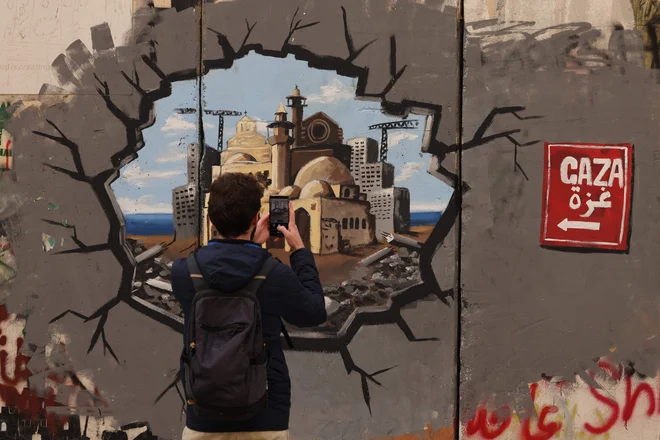 Moški fotografira grafit na delu izraelskega ločitvenega zidu v Betlehemu na okupiranem Zahodnem bregu, ki predstavlja obnovo Gaze. Posrednika Katarja in Egipta si prizadevata za rešitev krize v Gazi, je za AFP povedal palestinski vir, potem ko so Izrael in ZDA Hamasu naložile, naj ta konec tedna izpusti talce ali pa se bo vrnil v vojno. Foto: Hazem Bader/Afp
