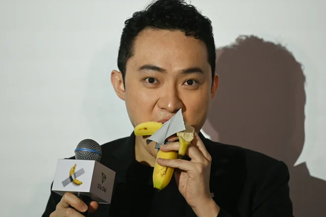Kriptomilijarder Justin Sun je za 6,2 milijona dolarjev kupil delo Comedian umetnika Maurizia Cattelana – banano, z lepilnim trakom prilepljeno na steno. Potem je banano pojedel. In vložil 75 milijonov dolarjev v kriptovaluto $Trump. FOTO: Peter Parks/AFP