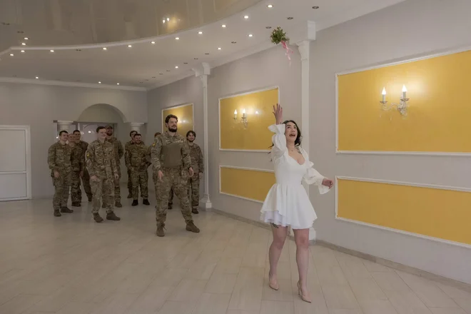 Anna meče šopek cvetja med poročnim obredom s Pavlom Čornobajem, ukrajinskim vojakom brigade Azov, na matičnem uradu v Slovjansku v vzhodni regiji Doneck. Vojna je dala občutek nujnosti zavezanosti ukrajinskih vojaških parov, ki ne vidijo smisla v čakanju na mir. Pogovori o premirju se v Slovjansku, približno 20 km od frontne črte zdijo daleč od realnosti. Zakonska zveza lahko varuje partnerje vojaškega osebja, saj so deležni socialne podpore in imajo zagotovljen klic, če so njihovi zakonci ubiti ali ranjeni. »Ne prelagajte ljubezni na pozneje, to je verjetno najpomembnejša stvar. Ne čakajte na pravi trenutek,« je dejala Anna. Foto: Roman Pilipey/Afp