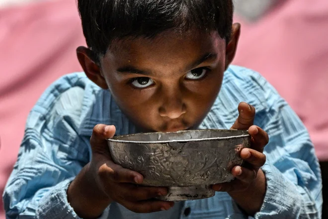 Deček pije vodo, ki jo v stari četrti Delhija razdeljuje pripadnik skupnosti Bhishti, tradicionalni prinašalec vode, na vroč poletni dan. Foto: Arun Sankar/Afp
