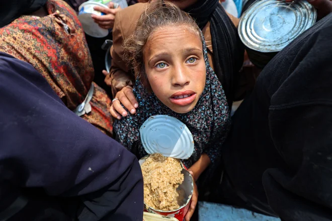 Palestinsko dekle čaka na obrok hrane na točki razdeljevanja hrane v begunskem taborišču Nuseirat v osrednjem delu območja Gaze. Čez mejni prehod Kerem Šalom je v Gazo končno vstopilo približno 90 tovornjakov s humanitarno pomočjo, ki so jo vendarle začeli razdeljevati, a je to, kot že dneve opozarjajo humanitarne organizacije, le kaplja v morje. Hudo lakoto trpi več kot dva milijona ljudi, pesti jih tudi kronično pomanjkanje pitne vode. FOTO: Eyad Baba/Afp