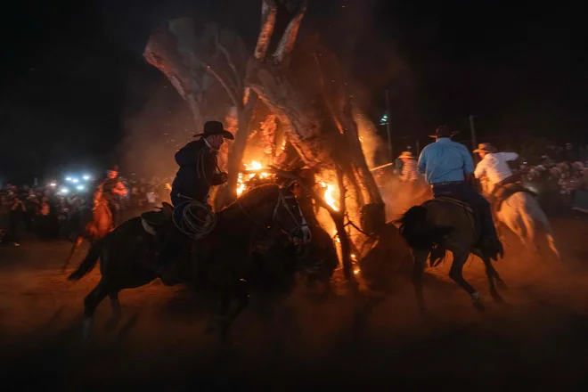 Kavboji s konji krožijo okoli kresa vokviru tradicionalne ognjene slovesnosti med praznovanjem »Fiesta en la Mision« v mehiškem mestu La Mision. Misijon San Miguel Arcangel, ki ga je leta 1787 ustanovil dominikanski menih Luis Sales, je bil namenjen evangelizaciji ljudstva Kumiai na severu države Baja California. Njegove ruševine, ki so še vedno vidne v kraju La Mision, označujejo ključno mesto na poti kolonialnih misijonov po Kaliforniji.  Foto: Guillermo Arias/Afp