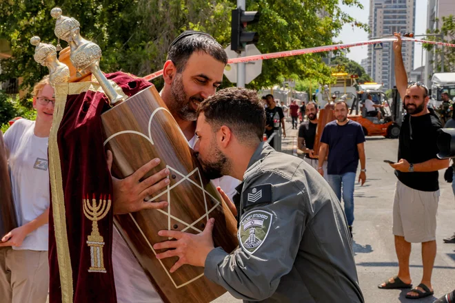Izraelski policist je poljubil enega od judovskih zvitkov Tore, potem ko so ga rešili iz sinagoge v osrednjem izraelskem mestu Holon, ki jo je danes zadela iranska raketa. Bolnišnica na jugu Izraela in dve mesti v bližini Tel Aviva so bili 19. junija zgodaj zjutraj prizadeti po soju iranskih raket, reševalci pa poročajo, da je bilo v zadnjih napadih ranjenih najmanj 47 ljudi. FOTO: Jack Guez/Afp
