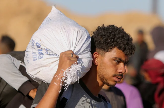 Palestinec nosi vrečo s pomočjo, ki jo je prejel od GHF. FOTO: Hatem Khaled/Reuters