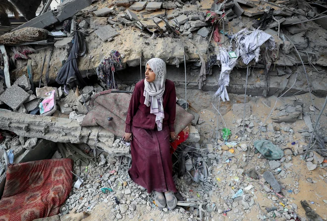 Palestinska ženska sedi sredi škode v šoli UNRWA, ki je bila prizadeta v izraelskem zračnem napadu v mestu Gaza. FOTO: Mahmoud Issa/Reuters