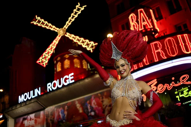 Plesalka kankana pred znamenitim kabarejem Moulin Rouge z obnovljeno vetrnico, na dan ponovne otvoritve 10. julija 2025. FOTO: Tom Nicholson/Reuters