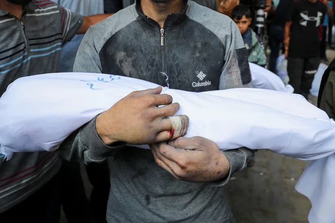 Oče nosi truplo Amirja, otroka, ubitega v izraelskem napadu. FOTO: Mahmoud Issa/Reuters