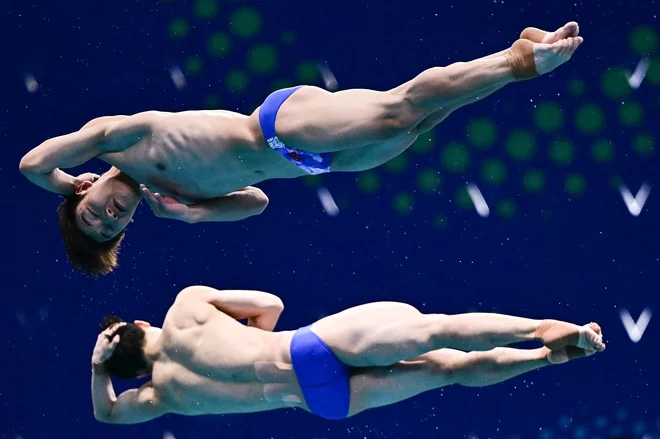 Kitajc Wang Zongyuan in Zheng Jiuyuan tekmujeta v finalu moškega sinhroniziranih skokov iz 3-metrske odskočne deske med svetovnim prvenstvom v vodnih športih v Singapurju. Foto: Manan Vatsyayana/Afp