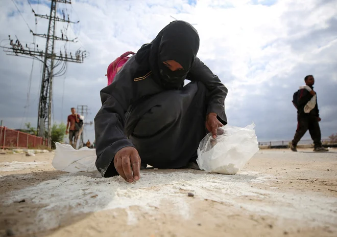 Prebivalka Gaze na mestu, kjer so razdeljevali pomoč, pobira raztreseno moko. FOTO: Reuters
