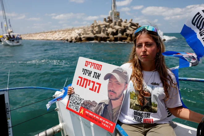 Ženska s sliko talca, medtem ko družinski člani talcev, ki jih držijo v Gazi, plujejo iz marine Aškelon do pomorske meje Gaze. FOTO: Amir Cohen/Reuters