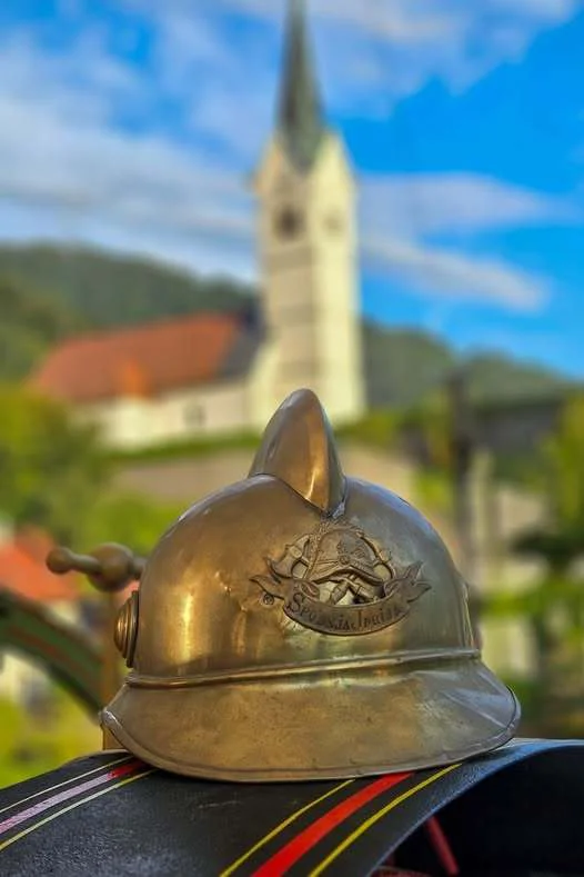 Gasilska čelada s spodnjeidrijsko cerkvijo v ozadju. FOTO: Robi Jereb
