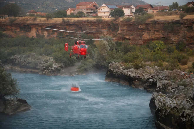 Po vsej Črni gori divja več obsežnih gozdnih požarov, zaradi katerih je tamkajšnja vlada zaprosila za pomoč tudi Nato in EU. Na fotografiji gasilski helikopter zajema vodo iz Morače v zaledju prestolnice Podgorica. Foto Stevo Vasiljevic/Reuters